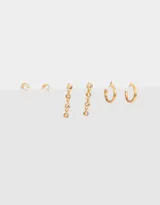 Set de tres pares de aros dorados bañados en oro con circonitas cúbicas. Incluye un par de aros tipo solitario, un par de aros colgantes con tres circonitas y un par de aros tipo argolla.