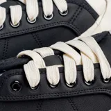 Zapatilla urbana negra con cordones blancos y suela blanca.