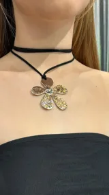 Gargantilla choker de doble tira de gamuza negra con dije de flor metálica dorada y plateada.