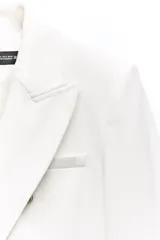 Blazer color blanco hueso, de corte entallado y doble botonadura dorada. Tiene cuello con solapa, mangas largas con hombreras y bolsillos delanteros con solapa.