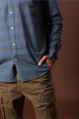 Camisa celeste con rayas horizontales en tonos beige y gris, de corte clásico, manga larga y cuello abotonado.