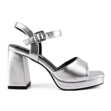 Sandalias plateadas de tacón ancho y plataforma, con tira sobre los dedos y pulsera con hebilla al tobillo.