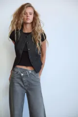 Pantalón de jean celeste de tiro alto, corte wide leg y largo hasta el tobillo. Presenta un diseño asimétrico en la cintura con cierre frontal cruzado con cremallera y botones metálicos.