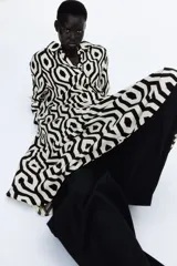 Vestido camisero midi de viscosa con estampado geométrico en blanco y negro. Tiene cuello camisero, tapeta de botones oculta, mangas largas raglán con puños sencillos y costuras fruncidas en la falda. Sin forrar.