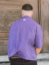 Camisa de manga corta con corte híbrido boxy fit/oversize, confeccionada en algodón. Disponible en tres diseños: a cuadros marrones, a rayas blancas y negras, y a rayas burdeos y blancas. Presenta bordados de diseño propio de la marca.