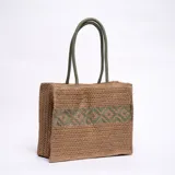Bolso tipo tote de yute color marrón claro, con diseño geométrico verde en el centro y doble asa de mano verde.
