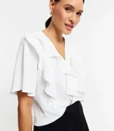 Camisa blanca de crepé con escote en V, mangas cortas y volados en el frente.