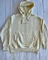 Hoodie color crema con capucha y cordón ajustable. Estampado en la espalda con un paisaje de montañas, árboles y un oso.
