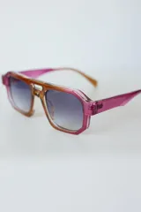 Lentes de sol de mujer con armazón grueso de policarbonato color rosa translúcido y lentes oscuros degradados. Diseño de montura geométrica con puente doble.