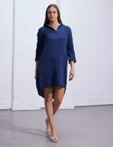 Vestido camisero blanco de algodón con cuello solapa, escote en V y mangas 3/4 regulables. Presenta bolsillos laterales verticales y abertura con botones en la espalda.