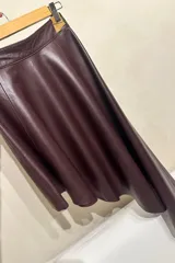 Falda corta color borgoña de cuero sintético, corte acampanado y diseño asimétrico.