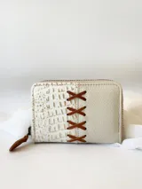 Billetera pequeña de cuero color crema, con cierre metálico y monedero interno. Presenta un diseño de cruces marrones en el frente y textura símil cocodrilo en un lateral.