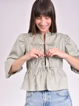 Blusa negra con escote mao y mangas 3/4 con volantes. Presenta detalle de frunces en el frente y lazos para ajustar.