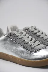 Zapatillas bajas color beige con detalles en marrón y cordones blancos.