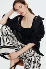 Pantalón largo de viscosa color blanco con estampado de flores y figuras geométricas en negro. Tiene tiro alto, cintura elástica con cordón ajustable, bolsillos laterales y corte holgado.