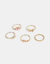 Set de 5 anillos dorados con dijes de flor rosa, mariposa con strass, hojas con strass rosa, strass blancos y un anillo entrelazado.