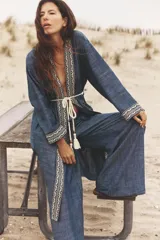Pantalón ancho azul con textura de lino, tiro alto, cintura elástica con cordón ajustable, pinzas delanteras, bolsillos laterales y traseros, y cinturón de la misma tela con apliques metálicos.