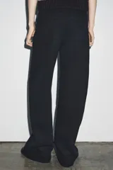 Pantalón de jean negro de corte palazzo, tiro medio y cintura con trabillas. Tiene bolsillos delanteros y traseros, raya planchada en el frente y cierre frontal con cremallera, botón y ganchos metálicos.