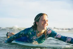 Entero de surf de lycra Ecocean reciclada con protección SPF 50, con estampa selvática en tonos azules y verdes, mangas largas azul brillante, escote en V y cierre frontal.