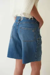 Bermuda de denim azul con tiro bajo, corte recto y largo hasta la rodilla. Presenta seis bolsillos, dos de ellos tipo cargo aplicados en el frente.