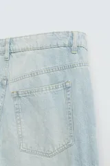 Pantalón de denim color beige, corte relaxed fit, con bolsillos laterales tipo cargo con solapa y cierre de botón. Cierre frontal con botón y cremallera.