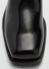 Bota alta de caña recta color negro charol, con apliques metálicos y punta cuadrada.