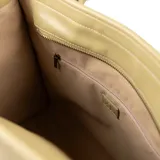 Bolso tipo tote grande color beige, confeccionado en cuero sintético. Tiene doble asa, una de mano trenzada y otra larga regulable para colgar del hombro. Incluye un dije metálico con el logo de la marca.