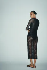 Vestido midi semitransparente de encaje negro, con escote recto, tirantes finos elásticos y mangas largas. Diseño drapeado en los laterales.