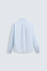 Camisa celeste a rayas verticales, de corte relaxed fit, confeccionada en lino y algodón. Tiene cuello abotonado, manga larga con puños abotonados, bolsillo de parche en el pecho y cierre frontal con botones.