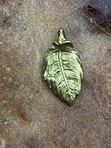 Dije de bronce con forma de hoja, modelado y tallado a mano.