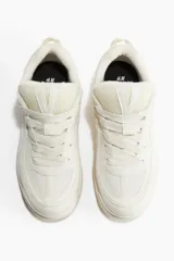 Zapatillas deportivas de estilo skate color crema, confeccionadas en malla y tejido revestido. Presentan cuello y lengüeta acolchados, cordones y trabilla trasera. Forro de tejido rizado y plantillas de piqué. Suela con diseño y grosor de 4,1 cm.