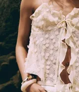 Blusa corta color crema, con lentejuelas y escote corazón. Tiene breteles finos ajustables, lazo en el busto y volados de chiffon.