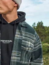 Canguro negro de manga larga con capucha, corte relajado y bolsillo tipo canguro. Estampado frontal con la inscripción "Originals Studio Brought to you by Jack&Jones Designed in Copenhagen".