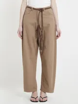 Pantalón color café de gabardina, corte relajado, con pinzas sutiles, bolsillos delanteros, cintura con presillas y cinturón de cuero fino con flecos.