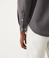 Camisa de hombre de manga larga, color gris oscuro, corte clásico, con cuello abotonado y cierre frontal con botones blancos.