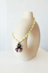 Collar corto con cuentas de plástico amarillas y verdes, y dije de vidrio con forma de pulpo negro.