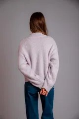 Buzo de punto color lila, con cuello redondo, mangas largas y diseño holgado. Presenta tres flores bordadas en el frente: una rosa claro, una azul y una amarilla con centro azul.