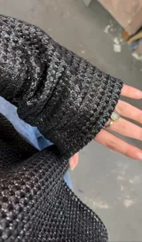 Blusa negra de tejido metalizado, con escote barco que puede usarse recto o caído en un hombro.