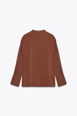 Camisa marrón de Zara Woman Collection confeccionada en hilatura con mezcla de lyocell. Tiene cuello redondo, manga larga acabada en puño, bajo asimétrico con aberturas laterales y cierre frontal con botones.