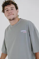 Remera gris de corte oversize con cuello redondo y estampado pequeño en el pecho con la frase "Karma Club" en color lila.