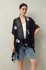 Poncho de gasa liviana color blanco, con bordados florales negros y detalles de borlas en el borde.