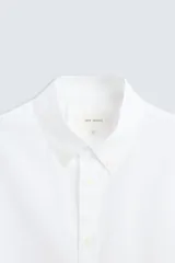 Camisa blanca de corte regular fit confeccionada en popelín de algodón. Tiene cuello abotonado, manga larga con puños abotonados y cierre frontal con botones.