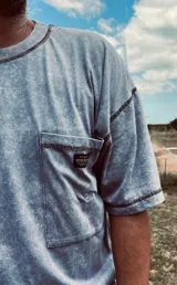 Remera gris con efecto gastado, cuello redondo, bolsillo en el pecho y costuras reforzadas.