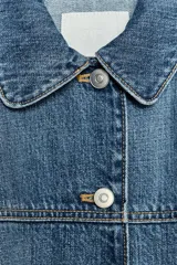 Cazadora de denim azul de corte holgado, con cuello solapa y manga tres cuartos acabada en puño. Cierre frontal con botones metálicos.