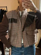 Campera corta con cuerpo a cuadros en tonos marrón, negro y beige, mangas largas tejidas en color marrón, detalles en cuero sintético negro en hombro y bolsillo, cierre frontal y bolsillos con solapa.