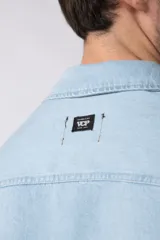 Chaqueta de jean celeste de corte recto, con cuello clásico, cierre frontal con botones metálicos y bolsillo de parche en el pecho.