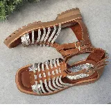 Sandalias bajas de cuero color beige con tiras horizontales plateadas y cierre con hebilla al tobillo.