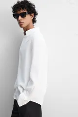 Camisa color arena de lino con cuello abotonado, manga larga con puños abotonados, corte regular y bajo con aberturas laterales.