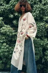 Vestido midi color crudo con bordados florales multicolores, escote en pico con lazos y mangas tres cuartos. Confeccionado en mezcla de algodón y lino.