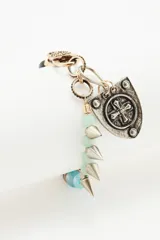 Pulsera de cuentas de piedras semipreciosas en tonos rojizos, negros y verde claro, con cierre de mosquetón dorado y un dije colgante en forma de escudo plateado con una cruz en relieve.